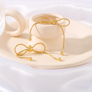 Elegant gold bow-shaped fringe earrings on a beige ceramic tray with white silk backdrop