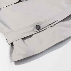 Detail of light gray trench coat cuff with black round button and woven texture