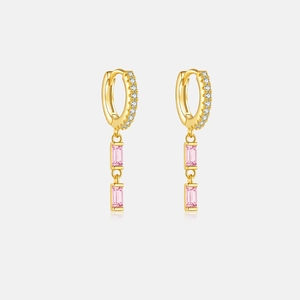 Macro detail of gold earrings with pink rectangular stones reflecting on a smooth surface