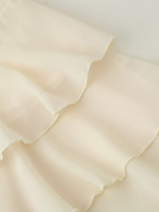 Dettaglio del tessuto in chiffon crema con eleganti volant stratificati e cuciture fini