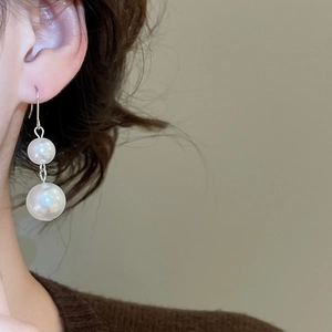 Close-up of elegant double pearl drop earrings with silver hooks on a female model
