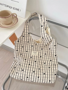 Chic cream canvas tote bag with black stripes and heart pattern on a modern chair