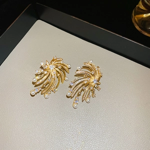 Detailed close-up of golden firework-shaped pearl earrings with sparkling zircons on a tray