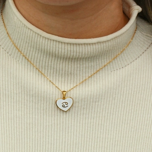 Close-up of golden heart pendant with Cancer zodiac symbol on a model wearing beige sweater