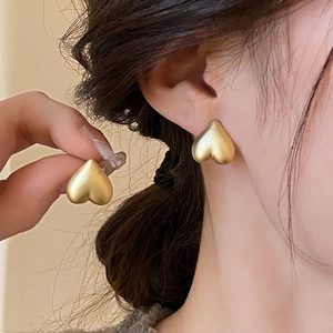 Macro shot of matte gold heart stud earrings showing elegant metallic finish