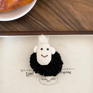 Detail of a handmade black sheep plush brooch with wool texture and bead eyes