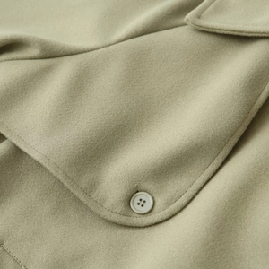 Close-up of sage green wool jacket featuring a buttoned pocket and detailed fabric texture