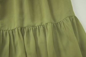 Détail de la texture du tissu en mousseline verte et de la couture de l'ourlet plissé