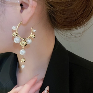 Detail of C-shaped drop earrings featuring dangling white pearls and golden metal fringe