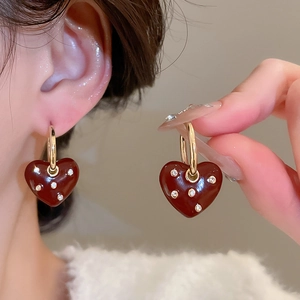 Macro detail of gold hoop earrings with red oil-drop heart pendants and small rhinestones