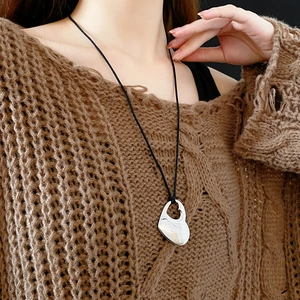 Close-up of a silver hollow double heart pendant necklace worn with a black cord strap
