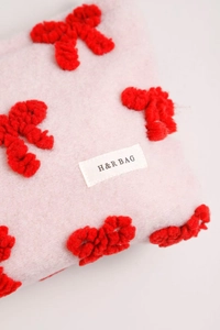 Close-up of pink plush makeup bag featuring 3D red ribbon and H&R BAG logo label