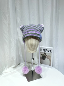 Detail of striped knit cat ear hat with metal pins, star patches and purple pom-poms