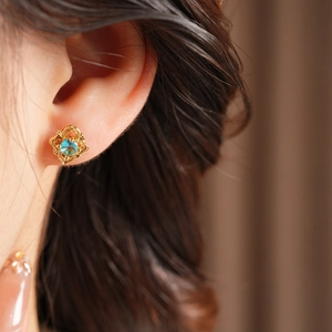 Close-up of vintage gold hollow earring with a central sky blue gemstone on a model