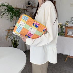 Detailed side view of a quilted floral patchwork makeup bag held in a hand