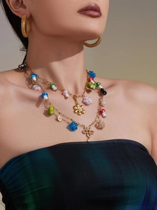 Detail of layered gold necklace with pearl flower, colorful mushroom charms and mesh earrings