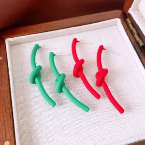 Detail of matte knot stud earrings in vibrant red and green colors on white fabric