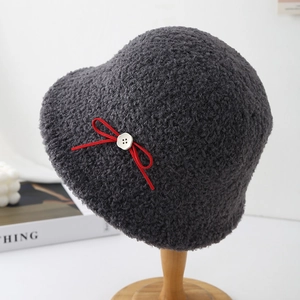 Detail view of a grey fuzzy sherpa bucket hat with a red bow and button accent