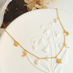 Elegant gold celestial necklace with star moon pendants and freshwater pearls on ceramic
