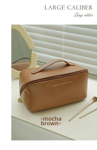 Mocha brown faux leather makeup bag with gold handle detail on a vanity desk