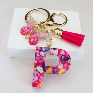Close-up of resin letter P keychain with pink butterfly, tassel, and gold accents