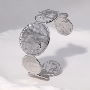 Macro detail of silver stainless steel cuff featuring textured hammered circular discs
