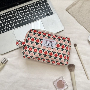 Corduroy cosmetic bag with tulip print next to laptop and makeup tools on a desk