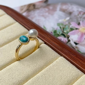 Detail of a gold ring featuring a lustrous white pearl and oval green turquoise stone