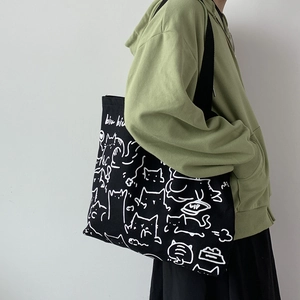 Detail of black canvas tote bag with cute white cat illustration and long shoulder strap