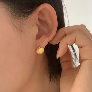 Close-up of a model wearing a gold shell-shaped earring with detailed scallop texture
