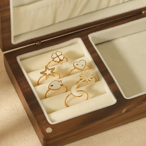Detailed close-up of six gold rings with white enamel clover and star in wooden jewelry box