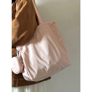 Pink nylon tote bag with small coin purse shown on shoulder in a minimalist setting