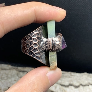 Macro detail of handmade copper ring featuring rectangular green stone and amethyst raw gem
