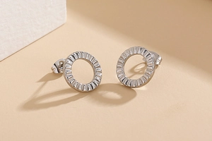 Close-up of silver geometric hoop earrings with radial texture on a minimalist display