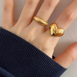 Detail of gold heart ring and textured band stacked on a woman's finger with a modern style