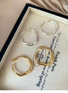 Detailed view of polished irregular wavy hoop earrings in gold and silver finish