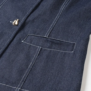Gros plan d'une poche de veste en jean bleu foncé avec coutures contrastées et bouton doré