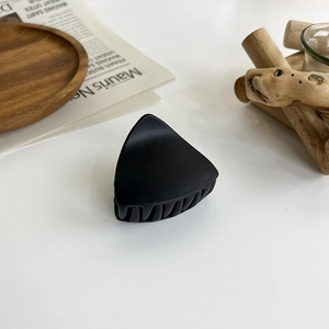Macro detail of matte black triangular hair claw clip on a minimalist aesthetic background