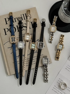 Close-up of square dial women's watch with rhinestone bezel on vintage books and perfume