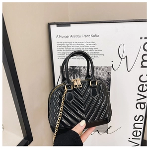 Detail showing black glossy jelly shell bag with V-shaped quilting and gold hardware