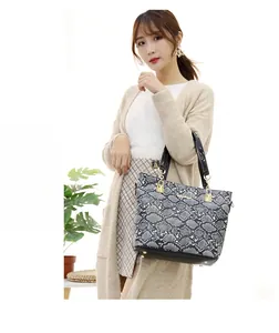 Detailed view of women's tote bag featuring snakeskin texture and black patent handles