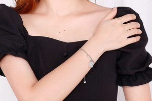 Detail of silver chain bracelet with rectangular pendant and heart charm on a female wrist