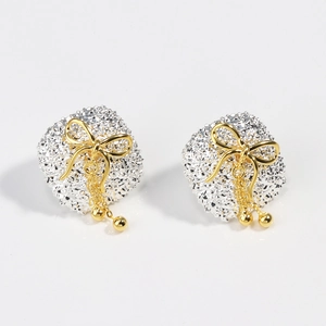 Detailed close-up of gold bow tassel earrings with a textured silver geometric square base
