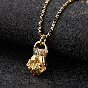 Macro view of gold fist pendant featuring detailed textures and a classic box chain