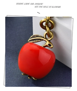 Detail of red apple keychain with glossy enamel finish and vintage gold metal leaf charm