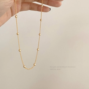 Vue macro détaillée d'un collier de perles dorées minimaliste tenu à la main sur fond neutre