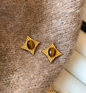 Détail de boucles d'oreilles vintage en œil de tigre sur un tissu en maille beige