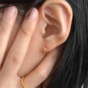 Minimalist small gold huggie hoop earring with high polish finish shown on ear