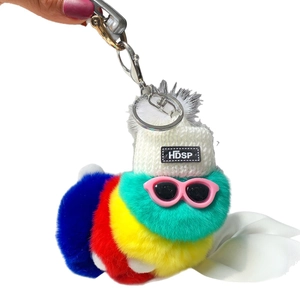Colorful plush caterpillar keychain with sunglasses and white knit hat held by a hand