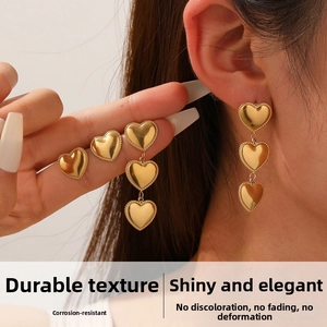 Detail of gold-plated stainless steel heart drop earrings with milgrain edge on model